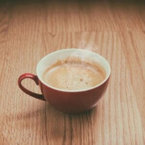 Steaming coffee in red cup on wooden table