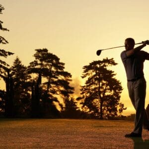Golfer silhouette swinging on sunset golf course