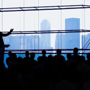 Silhouetted speaker addressing audience with city skyline