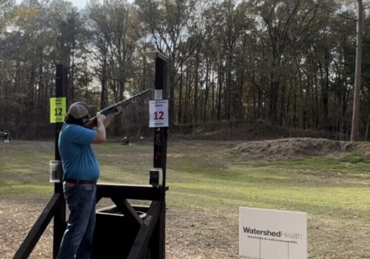 Person aiming shotgun at shooting range station.