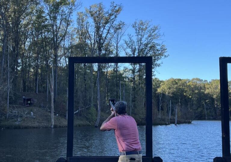 Man shooting from dock, lake and trees.